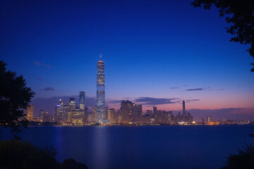 Naklejka premium City skyline at dusk with tall skyscraper and warm glow from setting sun