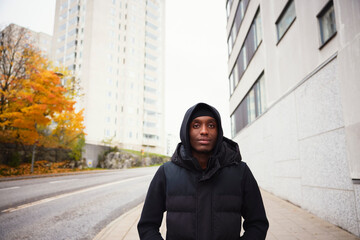 Young man wearing black jacket and standing against buildings