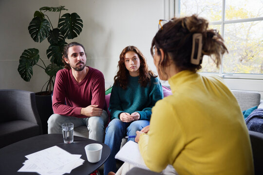 Father and daughter listening to female psychotherapist during session