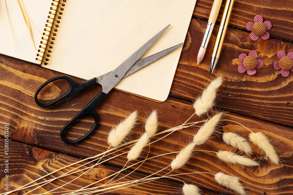 Poster crafting project setup with scissors, notebook, and decorative materials on wooden table