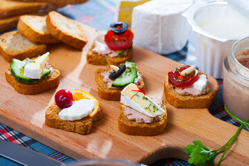Assorted homemade crostini appetizers with different filling served on wooden cutting board