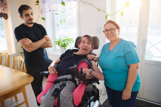 Portrait of happy female caregiver standing beside man with cerebral palsy sitting on wheelchair
