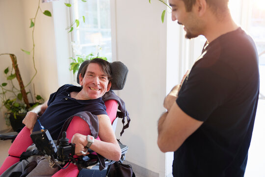 Portrait of happy man sitting on motorized wheelchair near male healthcare worker at nursing home