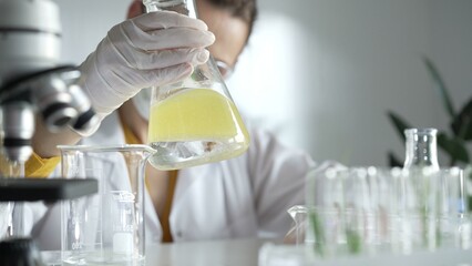 Woman scientist researcher wearing white protective gloves is shaking up a yellow chemical solution...