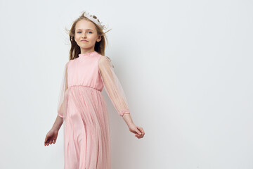 Elegant young girl in a light pink dress with a crown smiles softly, embodying innocence and joy...