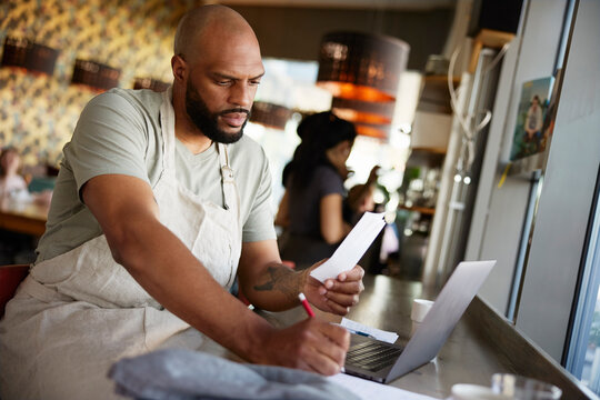 Male owner with shaved head examining financial bills while working at cafe