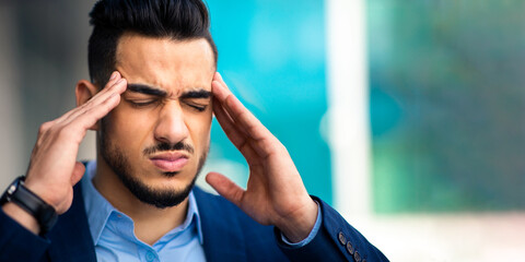 Closeup portrait of hard-working, stressed young arab businessman suffering from headache, standing...