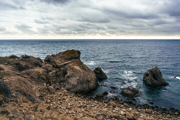 Rocky coastline under a dramatic sky with turbulent sea waves in the late afternoon