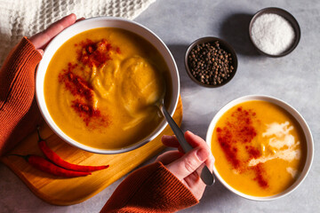 Woman tasting pumkin soup with spoon. Eating cream soup. High angle. Served table with soup bowl, pepper, chili, salt.