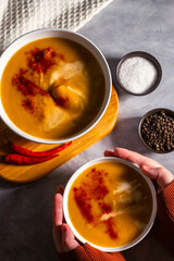 Woman holding bowl of pumkin soup with rusks. Served table with cream soup, chili pepper and napkin. Vegetable soup flat lay