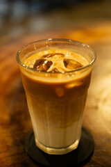 A refreshing iced latte served in a clear glass, placed on a wooden table, highlighting the contrast between the creamy coffee layers and the rustic wood texture