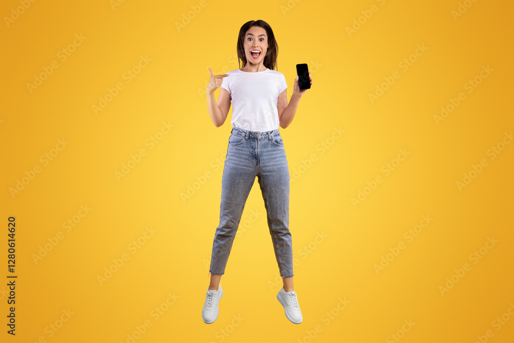 Poster cool mobile app. excited casual lady pointing finger at smartphone with blank screen and jumping up 