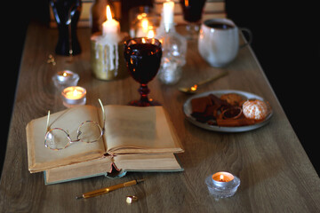 Books, lit candles, red wine, snacks and various deocration on the table. Dark academia or Halloween concept. Selective focus.