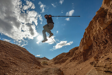 A man jumps off a cliff with hiking poles against the background of the sky and mountains, a photo...