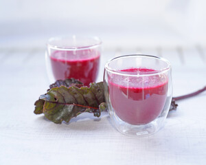 A cup of fresh beetroot juice with leaves on table.