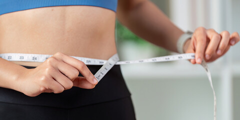 Woman measuring her waist with a tape measure, focusing on fitness and healthy lifestyle goals.