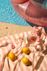 Sand with seashells, pink-striped towel, lemons, and rose drink, alongside gold accessories,...