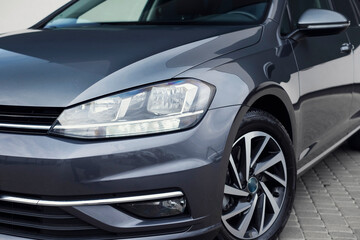 Modern compact dark gray car, with beautiful wheels, a large chrome radiator grill. Exterior details.