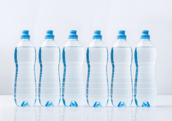 Naklejka premium Plastic bottles of water on a on a glossy white surface. Recyclable Pet containers for liquids.