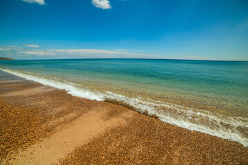 sea and beach with pebbles. sunny day, deserted beach and emerald calm water. Wide angle
