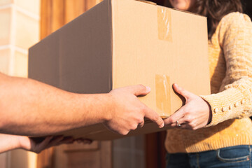 Hands Delivering Cardboard Package at Home Door. Package delivery concept, delivery worker and customer hands holding a cardboard box during the home delivery process.