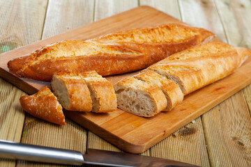 Freshly baked white baguette sliced on wooden background
