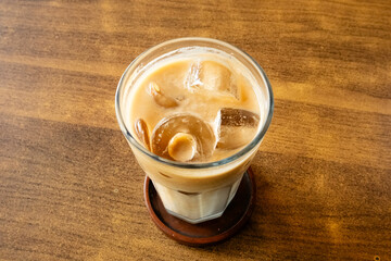 A refreshing iced latte served in a clear glass, placed on a wooden table, highlighting the contrast between the creamy coffee layers and the rustic wood texture