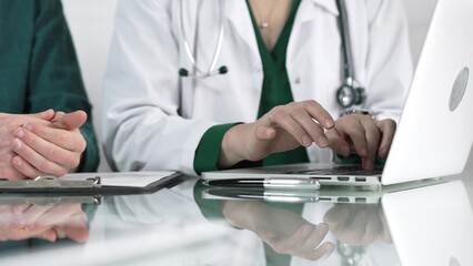 Doctor woman is typing on laptop computer while listening to patient complaints during medical consultation in clinic office. Medicine concept