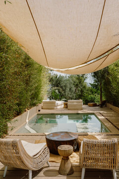 A serene outdoor pool area in Fethiye, T&uuml;rkiye, surrounded by lush greenery and shaded by a fabric canopy. Cozy white lounge chairs create a peaceful, nature-inspired retreat in a luxury setting