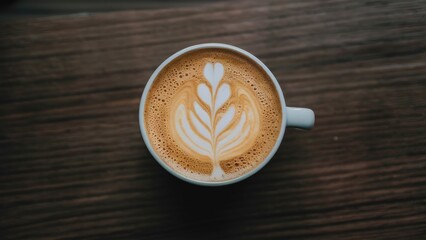Latte art depicting a leaf design in a white cup atop a dark wooden surface with warm tones creating a cozy atmosphere.