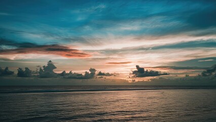 Naklejka premium Serene summer sunset over tranquil water horizon showcasing vibrant blue and orange hues with scattered clouds creating a picturesque evening view