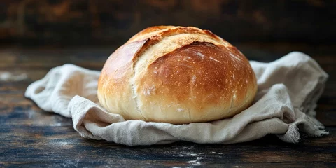 Round loaf of freshly baked bread on a light beige linen napkin positioned on a dark textured wooden surface with a rustic backdrop