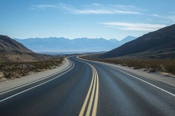 Winding Asphalt Road Through Desert Hills Leading Towards Distant Blue Mountains and Clear Sky