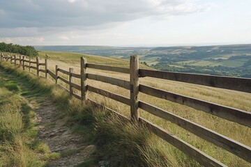 Fototapeta premium Rustic Wooden Fence Along Grassy Pathway Overlooking Rolling Green Fields Under Cloudy Sky