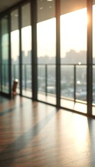 The sun shines through large windows in an empty room with wood floors.