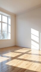 An empty room with white walls and light-colored wood floors illuminated by sunlight streaming through windows.