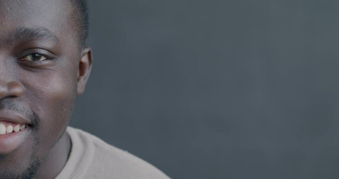 Portrait of African American man half face looking at camera smiling on black color background. People and good mood concept.