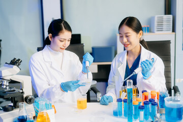 Two Asian female scientists in a high-tech lab analyzing biochemical samples, using micro pipettes,