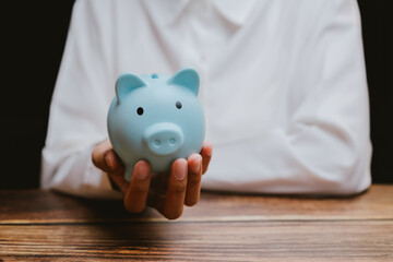 Person Holding Blue Piggy Bank on Wooden Table in Soft Lighting