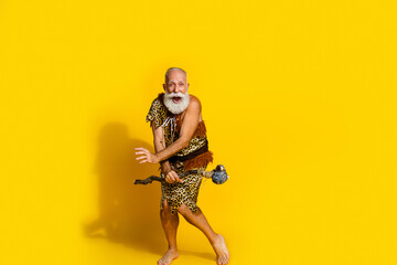 Photo of excited old caveman dancing energetic hold rock tool have fun isolated yellow color background
