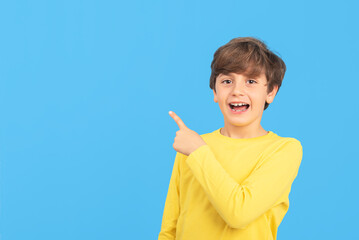 Happy young man smiling pointing finger to the side, in yellow sweater, cheerful facial expression, positive emotion, isolated on blue background