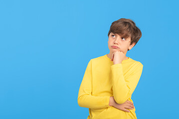 Thoughtful young boy looking to the side, hesitant, confused, pensive, in yellow sweater, isolated on blue background