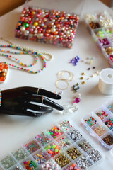 Hand figurine, colorful friendship bracelets, necklaces, various beads and DIY supplies on the table. Making jewelry at home. Selective focus.