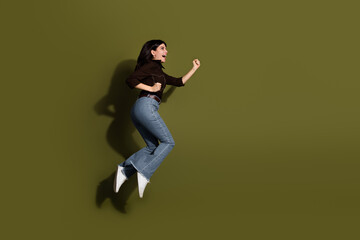 Jumping woman in casual outfit with khaki background showing joyful expression and energy