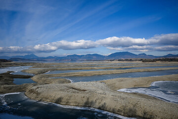 A picturesque view of the drying bottom of Liptovská Mara with exposed sandy areas, remnants of ice and mountains in the background under a cloudy sky