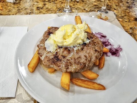 Top view of grilled balkan pljeskavica with kajmak cheese, served with fries in a traditional serbian restaurant in Zlatibor, Serbia