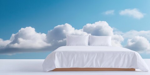 A white bed with pillows and a blue sky background. The bed is empty and the sky is full of clouds
