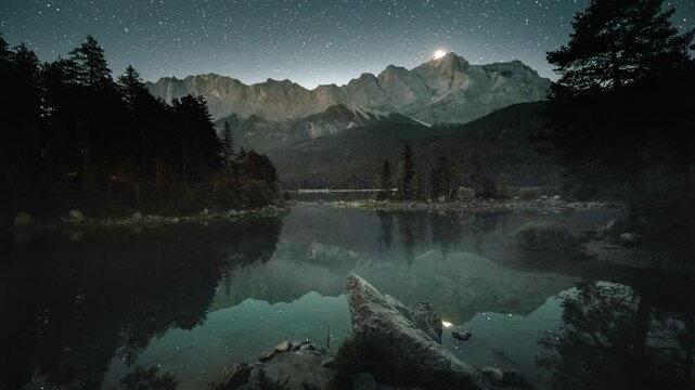 Mountain lake time lapse from night to morning, with stars and sun and the Alps. A gorgeous landscape at Eibsee in Bavaria, Germany. 
