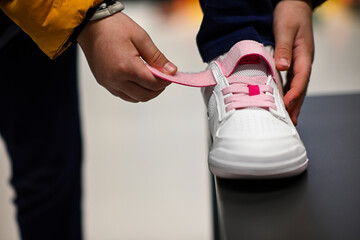 Close-up of hands fastening velcro strap on child's white shoe with pink laces in a shoe store