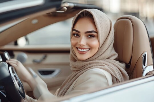 Excited muslim woman in hijab testing new luxury car, sitting on front seat half-turned back and smiling at camera